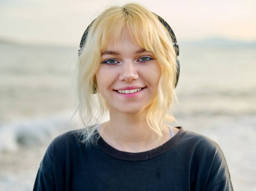 Portrait of smiling teenage female wearing headphones, on beach, close-up face, smile with teeth